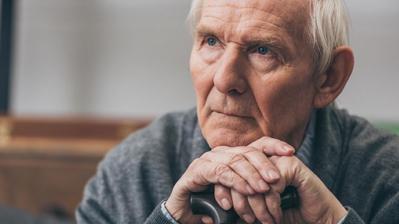 Older man in thoughtful pose holding cane